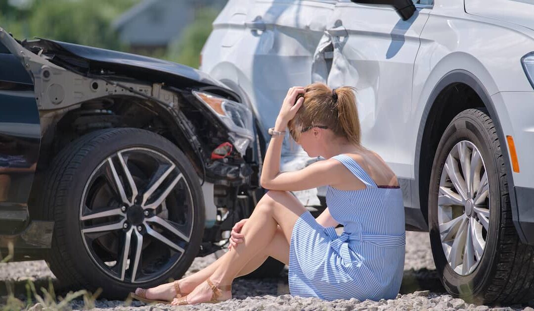 Woman sitting beside damaged cars after an auto accident, experiencing distress, highlighting the need for chiropractic care for accident injuries and pain relief.